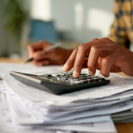 Realistická detailná fotografia rúk používajúcich kalkulačku na stole plnom účtovných dokumentov, faktúr